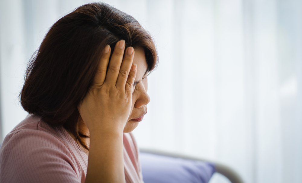 A woman sits with her hand on her head, likely in pain from brain injury