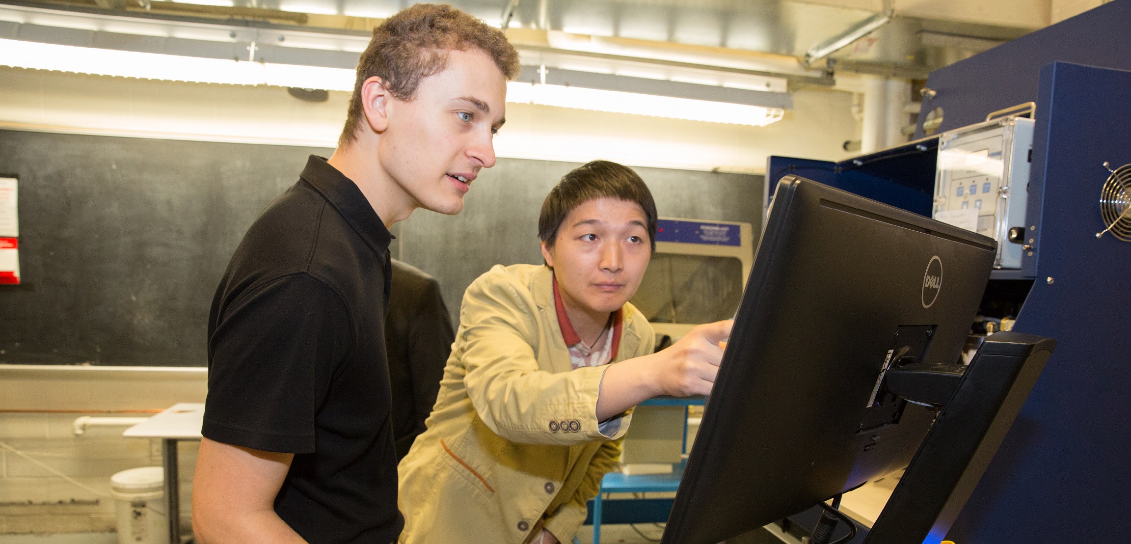 Two people pointing at a monitor in the lab 