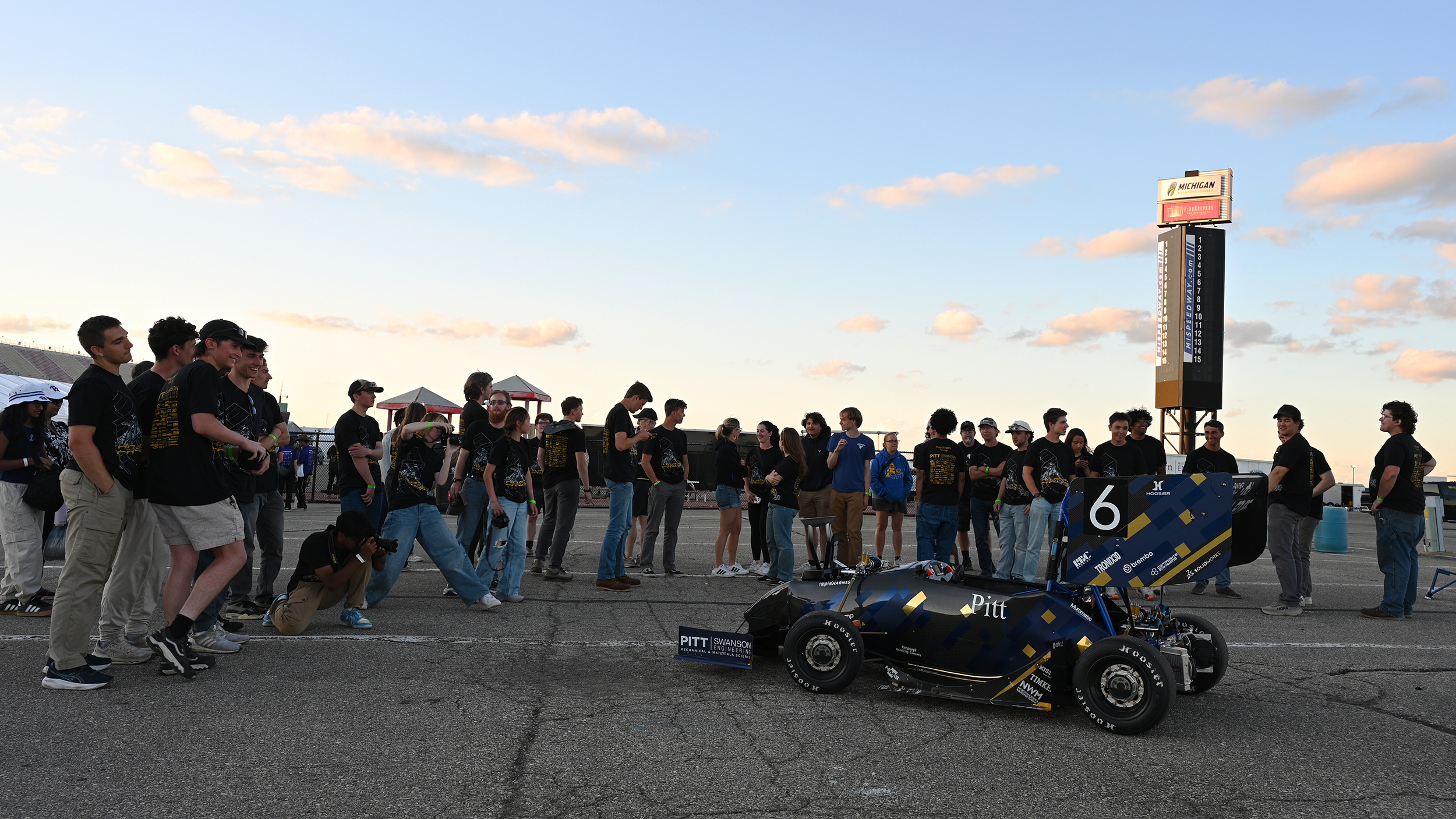 The Panther Racing team together on the tarmac in Michigan with the car in the foreground.