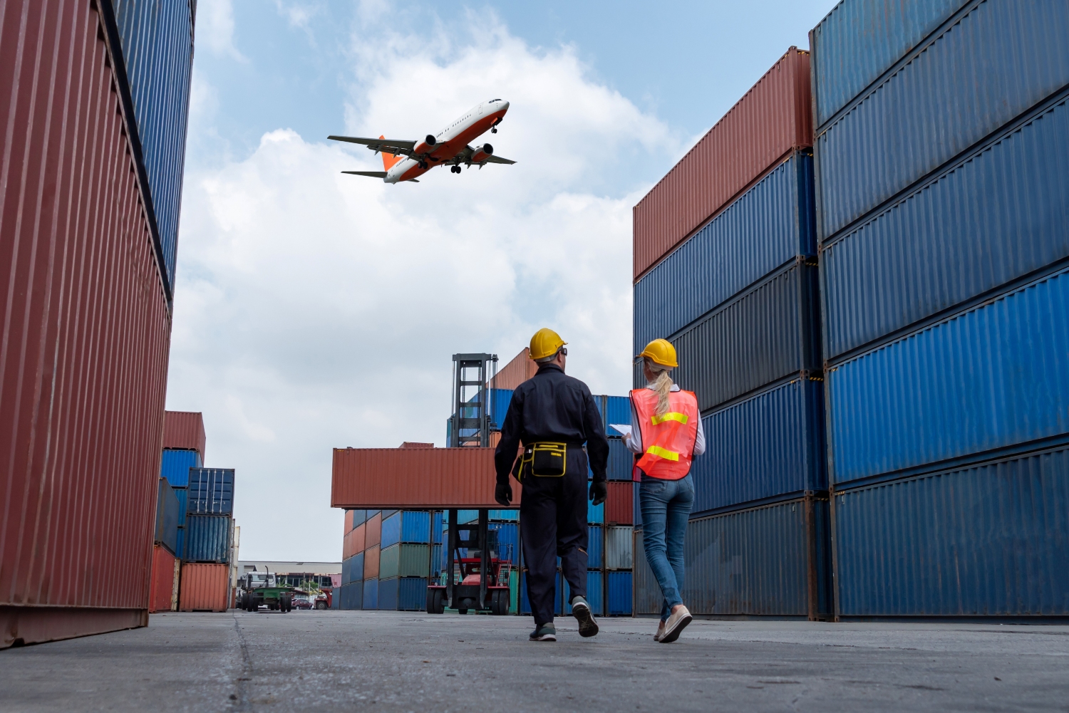 Two engineers at a shipping container port with a plane flying overhead