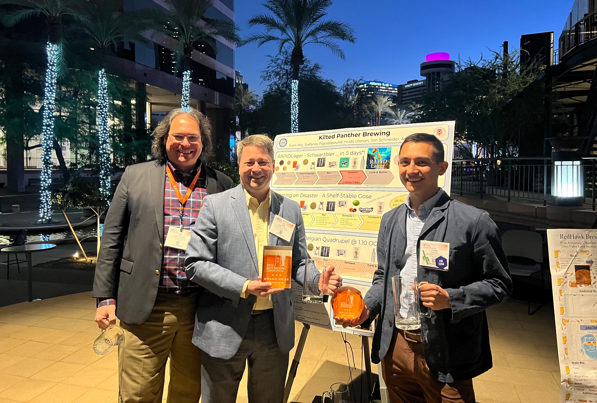 3 brU members holding 2 awards and standing by the 2022 competition poster